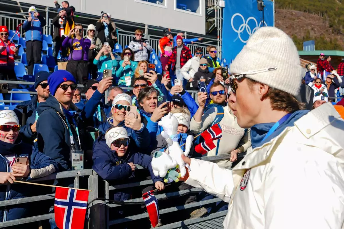 Johannes Hoesflot Klaebo, of Norway, gives his Tina mascot tooth to fans on the stands after winning the gold medal in the cross country skiing men's 4 x 7.5km relay at the 2026 Winter Olympics, in Tesero, Italy, Sunday, Feb. 15, 2026. (AP Photo/Kirsty Wigglesworth)