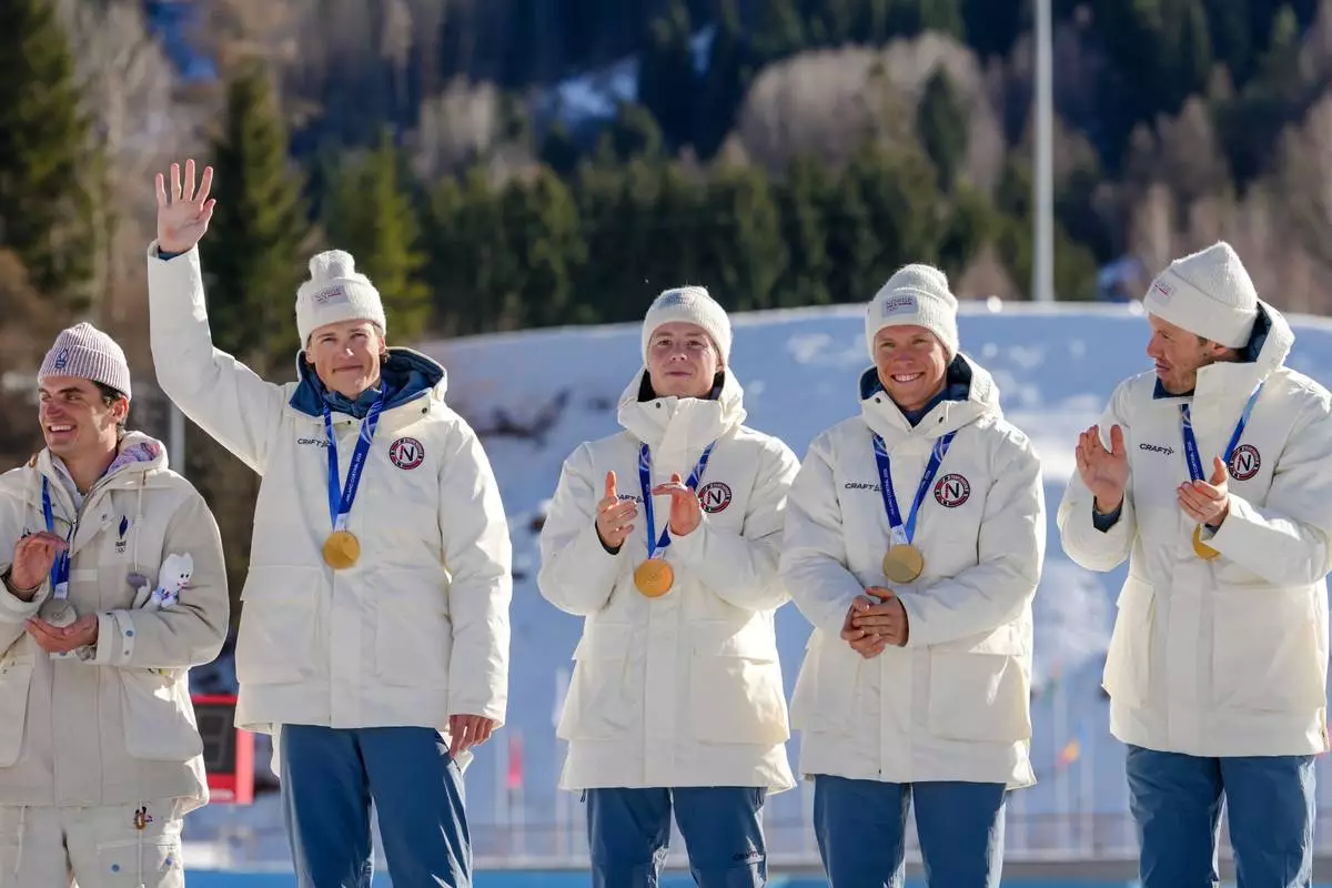 Johannes Hoesflot Klaebo, of Norway, waves from the podium, with teammates Einar Hedegart, Martin Loewstroem Nyenget and Emil Iversen, after winning the gold medal in the cross country skiing men's 4 x 7.5km relay at the 2026 Winter Olympics, in Tesero, Italy, Sunday, Feb. 15, 2026. (AP Photo/Kirsty Wigglesworth)
