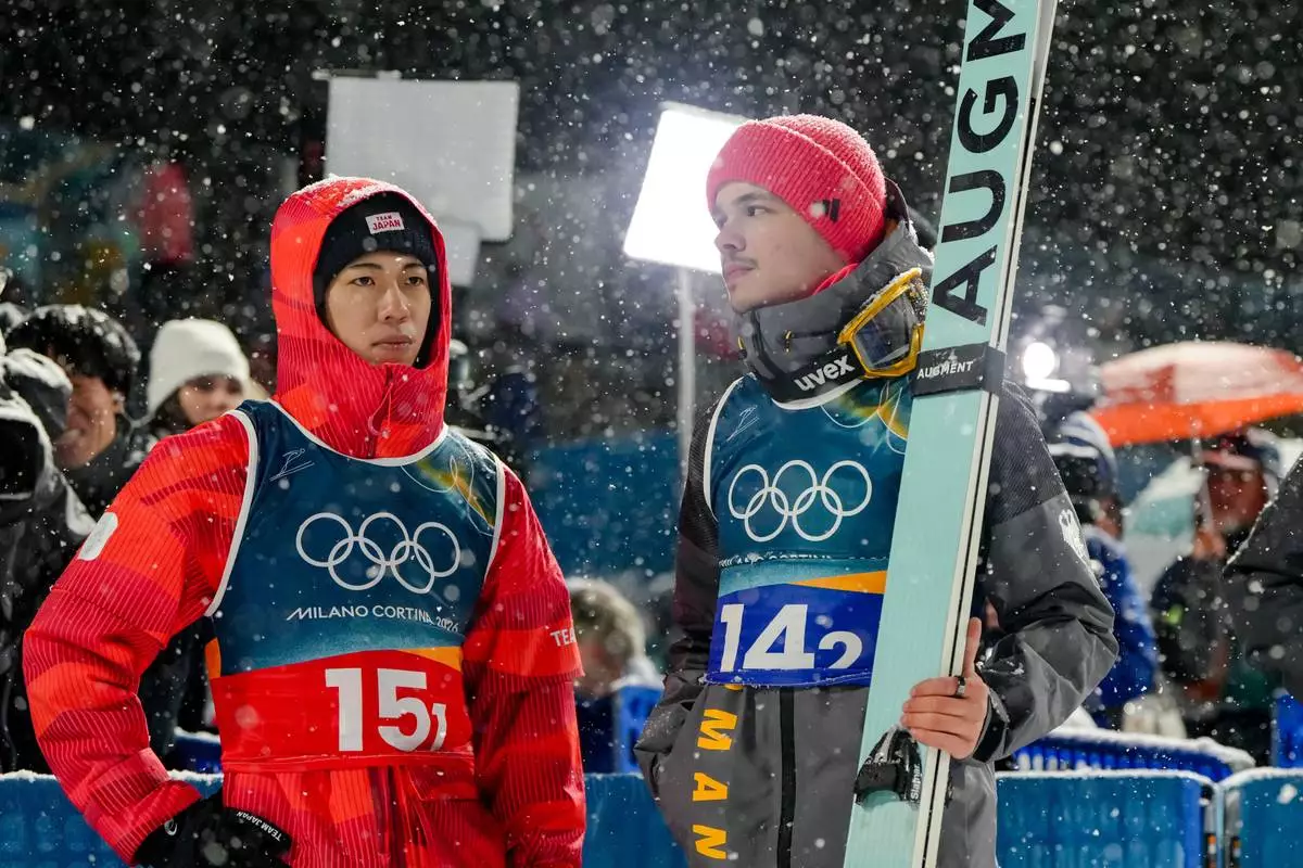 Ren Nikaido, of Japan, left, and Philipp Raimund, of Germany, react as a snowfall interrupts the final round jump of the ski jumping men's super team competition at the 2026 Winter Olympics, in Predazzo, Italy, Monday, Feb. 16, 2026. (AP Photo/Kirsty Wigglesworth)