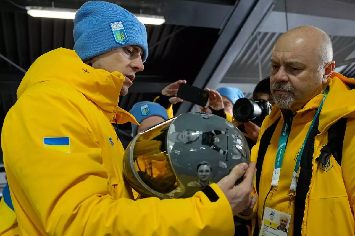 Ukrainian skeleton athlete Vladyslav Heraskevych left, holds his crash helmet at the mixed zone of the sliding center at the 2026 Winter Olympics, in Cortina d'Ampezzo, Italy, Thursday, Feb. 12, 2026. (AP Photo/Alessandra Tarantino)