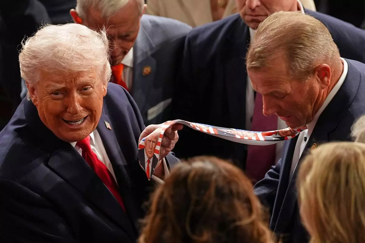 FILE - President Donald Trump holds up a tie designed with his face, worn by Rep. Troy Nehls, R-Texas, as he exits the House chamber after delivering the State of the Union address at the U.S. Capitol in Washington, Feb. 24, 2026. (AP Photo/Matt Rourke, File)