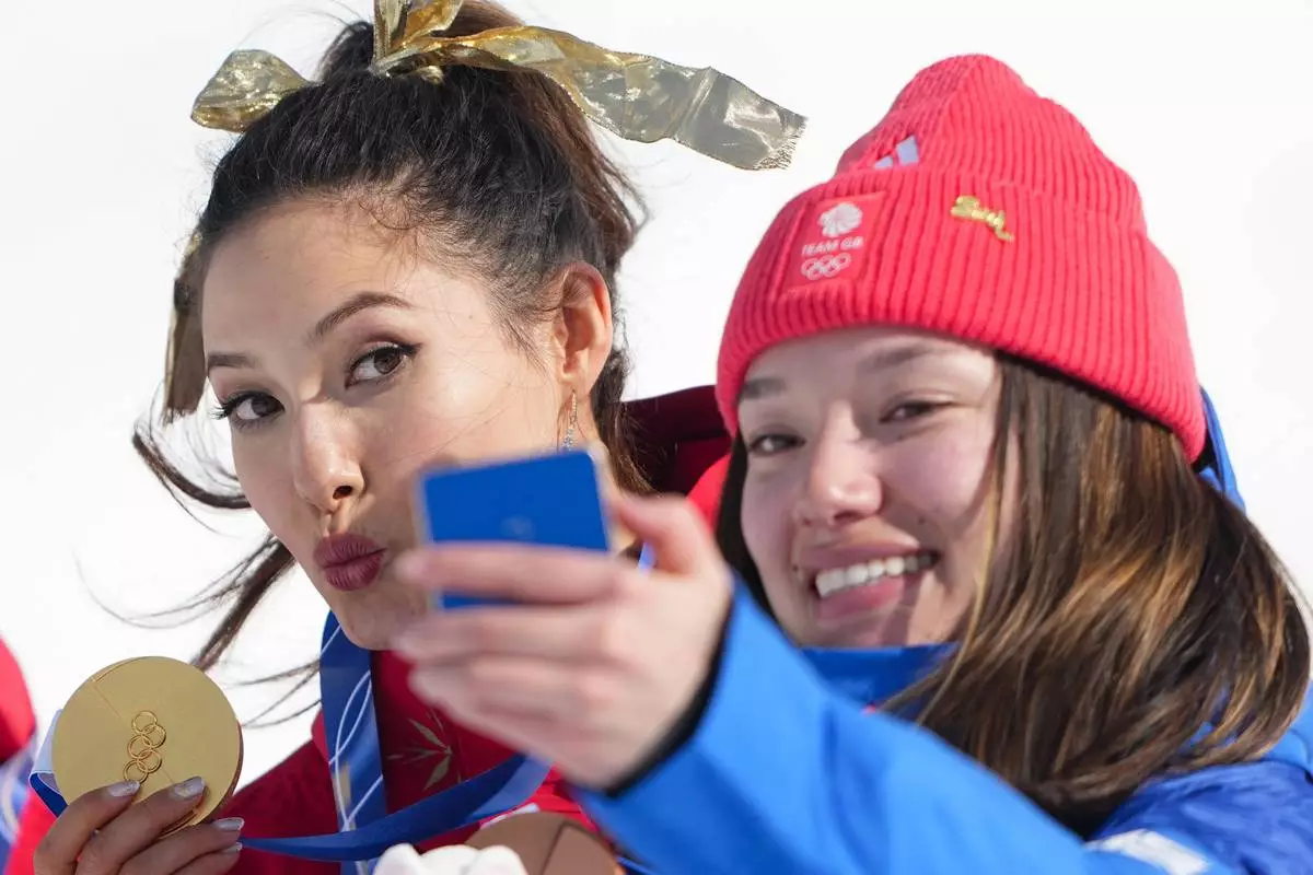 Gold medalist China's Eileen Gu and bronze medalist Britain's Zoe Atkin, right, take a selfie after the women's freestyle skiing halfpipe final at the 2026 Winter Olympics, in Livigno, Italy, Sunday, Feb. 22, 2026. (AP Photo/Lindsey Wasson)