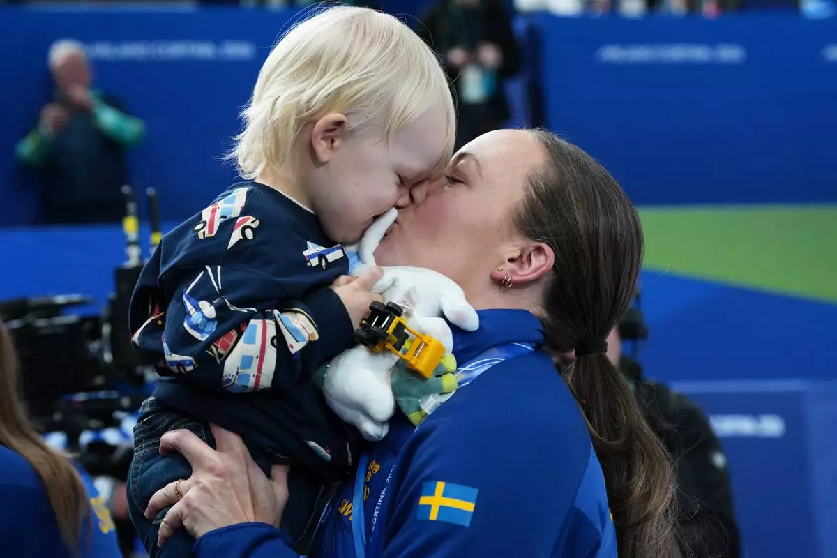 Sweden's Sofia Scharback holds her child after winning the gold medal of the women's curling, at the 2026 Winter Olympics, in Cortina d'Ampezzo, Italy, Sunday, Feb. 22, 2026.(AP Photo/Misper Apawu)