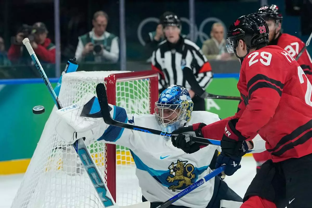 Finland's Juuse Saros (74) makes a save in front of Canada's Nathan MacKinnon (29) during a men's ice hockey semifinal game between Canada and Finland at the 2026 Winter Olympics, in Milan, Italy, Friday, Feb. 20, 2026. (AP Photo/Petr David Josek)