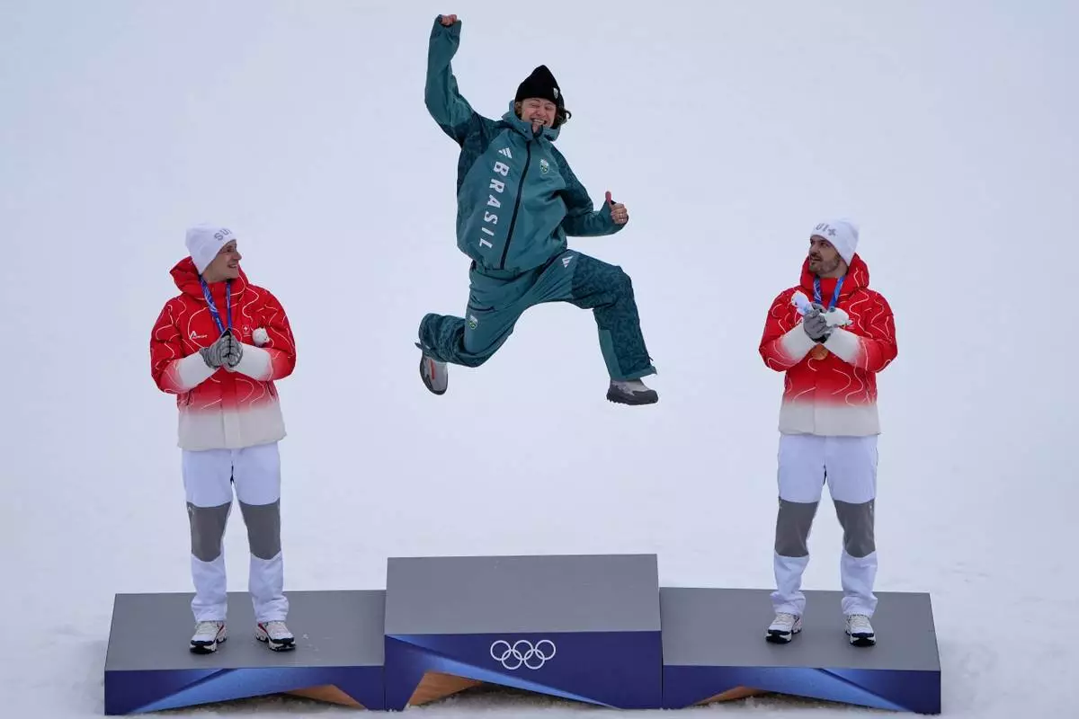 Brazil's Lucas Pinheiro Braathen, center, winner of an alpine ski, men's giant slalom race, jumps in celebration on the podium flanked by second placed Switzerland's Marco Odermatt, left, and third placed Switzerland's Loic Meillard, at the 2026 Winter Olympics, in Bormio, Italy, Saturday, Feb. 14, 2026. (AP Photo/John Locher)