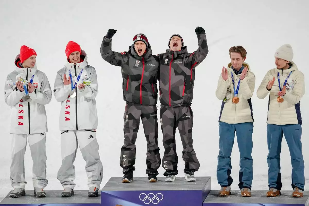 Gold medalists Stephan Embacher and Jan Hoerl, of Austria, celebrate on the podium, with silver medalists Pawel Wasek and Kacper Tomasiak, of Poland, and bronze medalists Kristoffer Eriksen Sundal and Johann Andre Forfang, of Norway, after the ski jumping men's super team competition at the 2026 Winter Olympics, in Predazzo, Italy, Monday, Feb. 16, 2026. (AP Photo/Matthias Schrader)