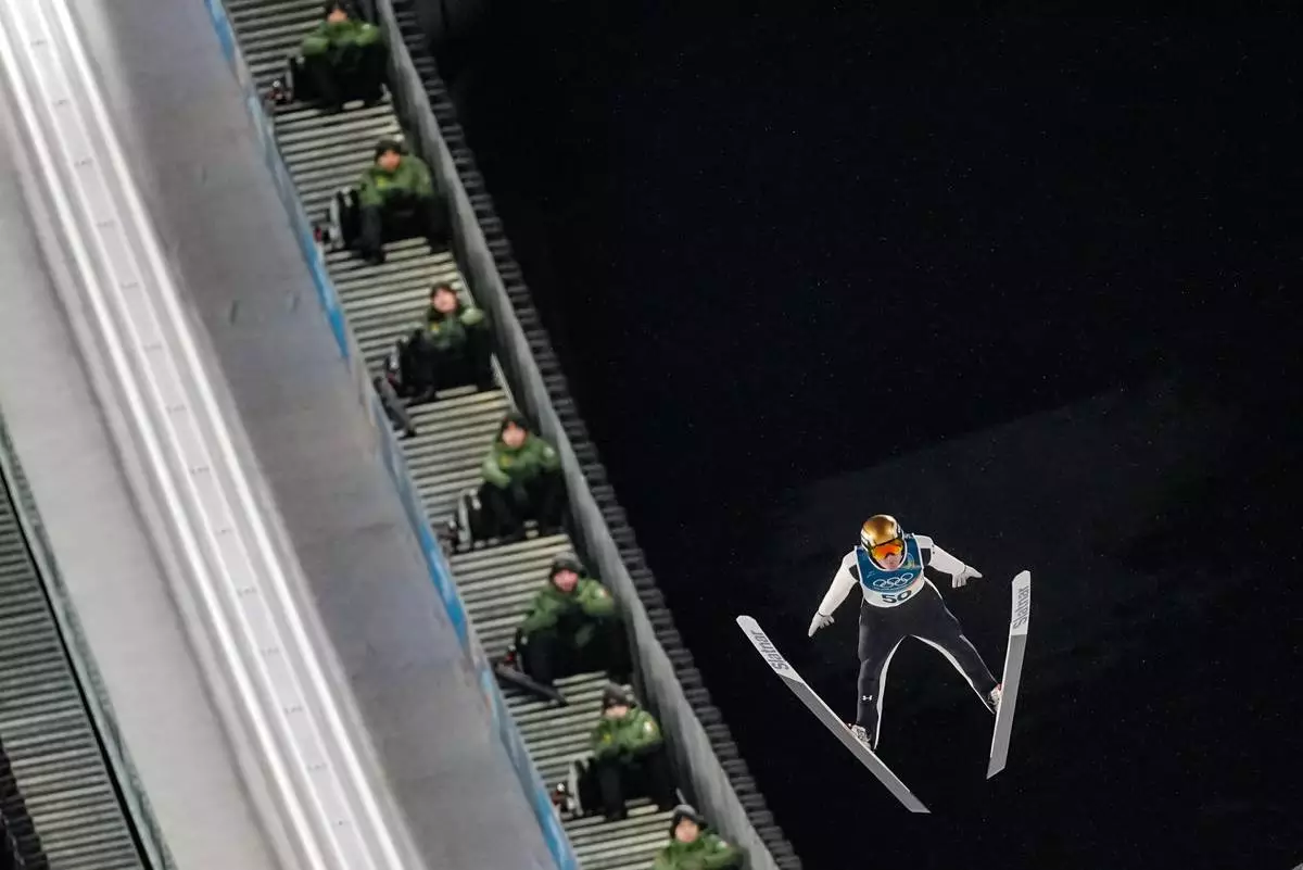 Italian Army soldiers on the steps of the ramp watch Domen Prevc, of Slovenia, soaring through the air during his first round jump of the ski jumping men's large hill individual at the 2026 Winter Olympics, in Predazzo, Italy, Saturday, Feb. 14, 2026. (AP Photo/Matthias Schrader)