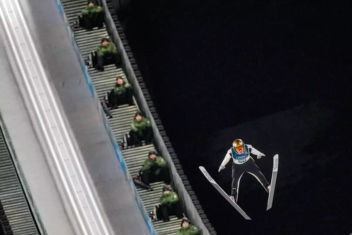 Italian Army soldiers on the steps of the ramp watch Domen Prevc, of Slovenia, soaring through the air during his first round jump of the ski jumping men's large hill individual at the 2026 Winter Olympics, in Predazzo, Italy, Saturday, Feb. 14, 2026. (AP Photo/Matthias Schrader)