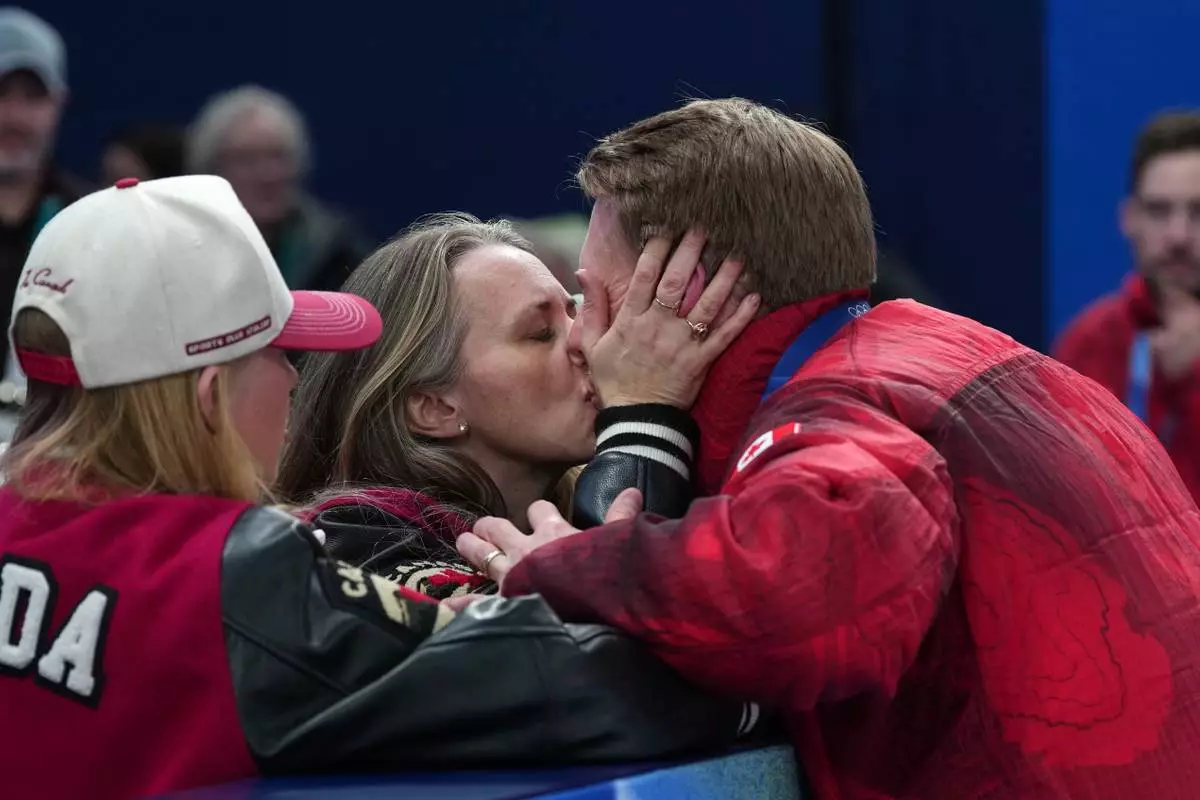 Canada's Marc Kennedy, right, exchanges a kiss as he celebrates winning a men's curling gold medal match between Britain and Canada, at the 2026 Winter Olympics, in Cortina d'Ampezzo, Italy, Saturday, Feb. 21, 2026. (AP Photo/Misper Apawu)