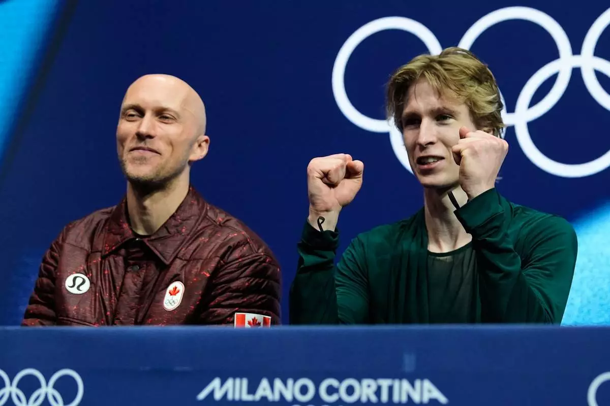 Stephen Gogolev of Canada, right, reacts to his scores after competing during the men's free skate program in figure skating while sitting next to choreographer Benoit Richaud, left, at the 2026 Winter Olympics, in Milan, Italy, Friday, Feb. 13, 2026. (AP Photo/Ashley Landis)