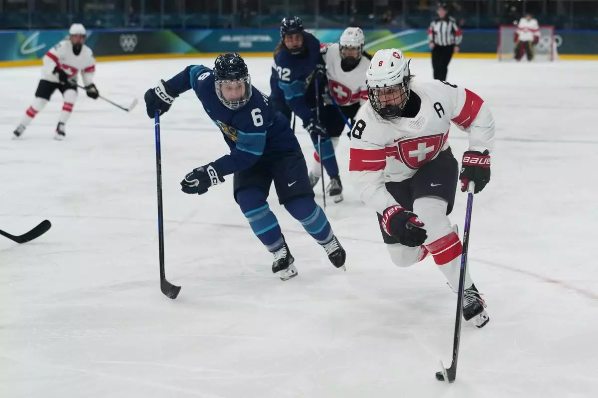 Switzerland's Kaleigh Quennec (8) skates with the puck as Finland's Jenni Hiirikoski (6) chases in the first during a preliminary round match of women's ice hockey at the 2026 Winter Olympics, in Milan, Italy, Tuesday, Feb. 10, 2026. (AP Photo/Carolyn Kaster)