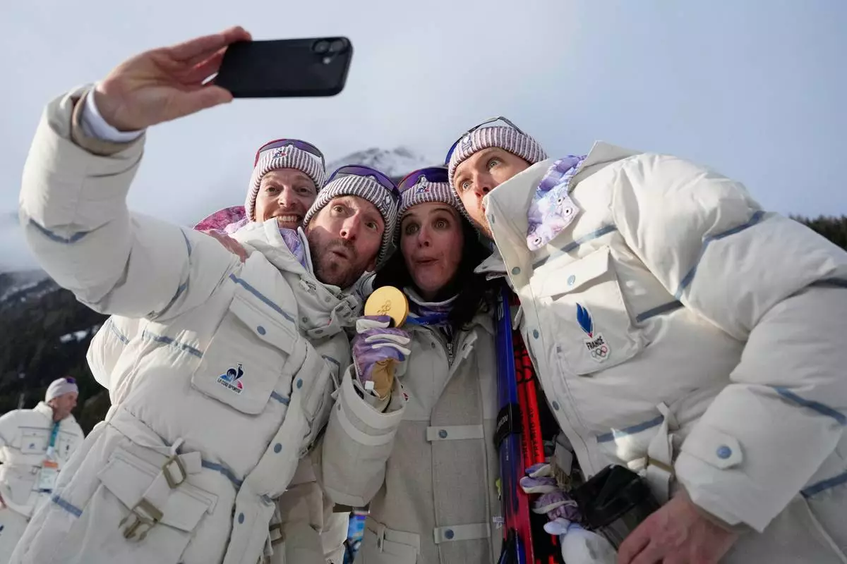 Julia Simon, of France, center, poses for a selfie with the gold medal for the women's 15-kilometer individual biathlon race at the 2026 Winter Olympics in Anterselva, Italy, Wednesday, Feb. 11, 2026. (AP Photo/Mosa'ab Elshamy)
