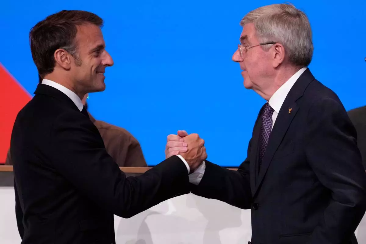 FILE - IOC president Thomas Bach, right, shakes hands to French President Emmanuel Macron after Bach announced that the French Alps was named as the 2030 Winter Games host at the 2024 Summer Olympics, Wednesday, July 24, 2024, in Paris, France. (AP Photo/David Goldman, File)