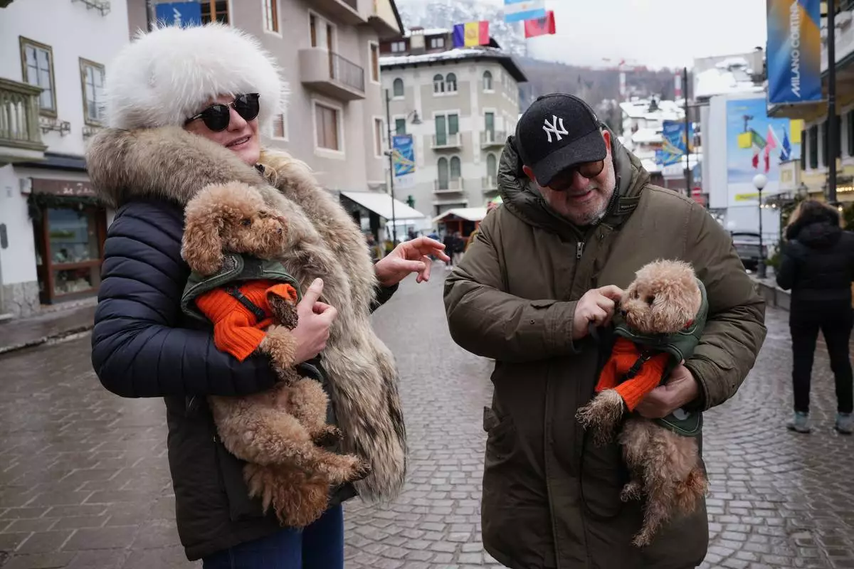 Husband and wife, Christina and Roberto, pose for a photo with their poodles, Gualtiero, left, and Leone, wearing customised Loro Piana jackets, in Cortina d'Ampezzo, Italy, on Saturday, Feb. 14, 2026. (AP Photo/Alessandra Tarantino)