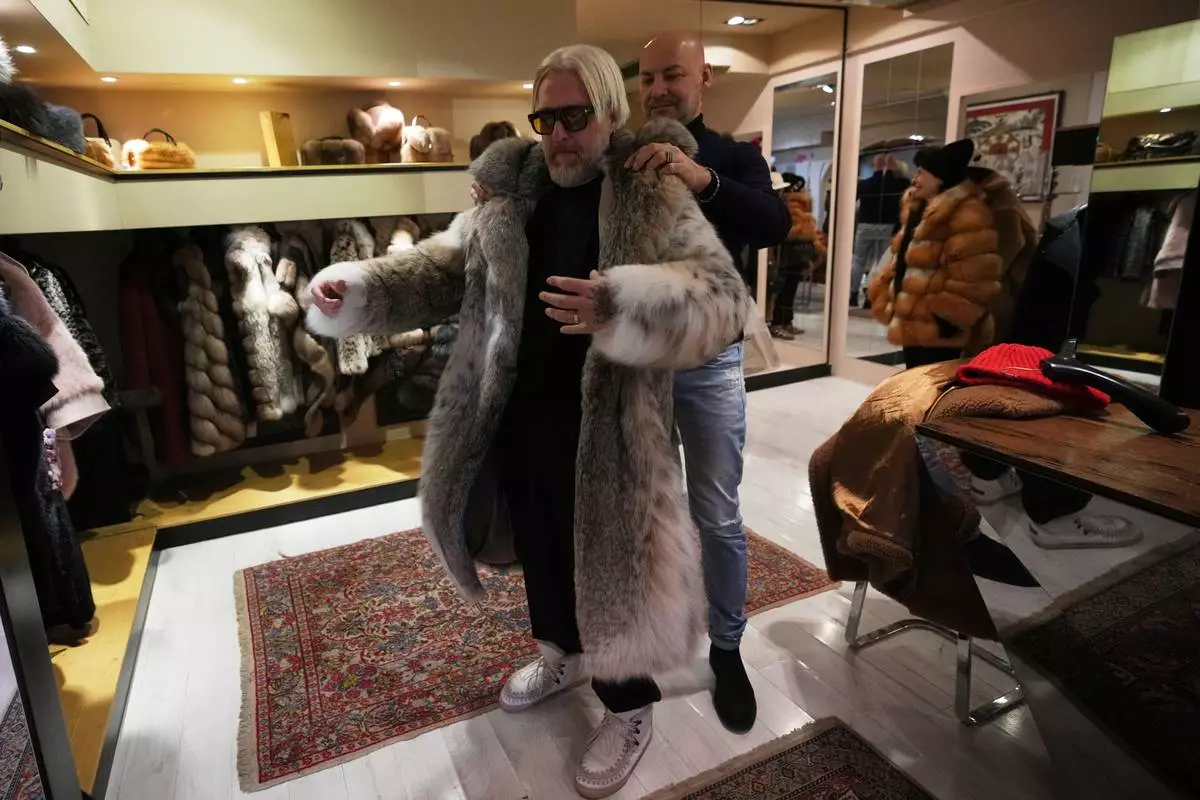 Sales manager for Pajaro, a luxury Italian fashion brand, Marco Molinari, right, helps his client, Stefano Vannicola, put on a fur coat in Cortina d'Ampezzo, Italy, Saturday, Feb. 14, 2026. (AP Photo/Alessandra Tarantino)