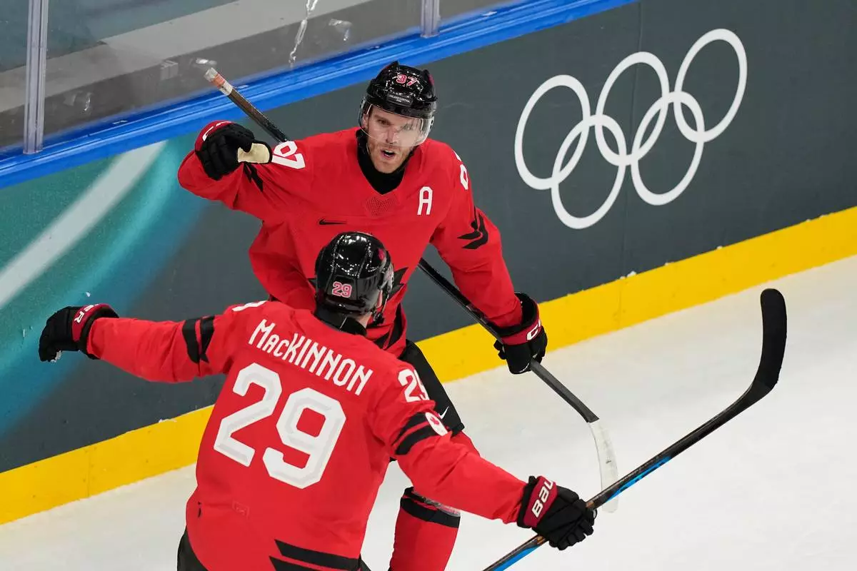 Canada's Connor McDavid, back, celebrates with Canada's Nathan MacKinnon after scoring his sides first goal during a preliminary round match of men's ice hockey between Canada and Switzerland at the 2026 Winter Olympics, in Milan, Italy, Friday, Feb. 13, 2026. (AP Photo/Hassan Ammar)