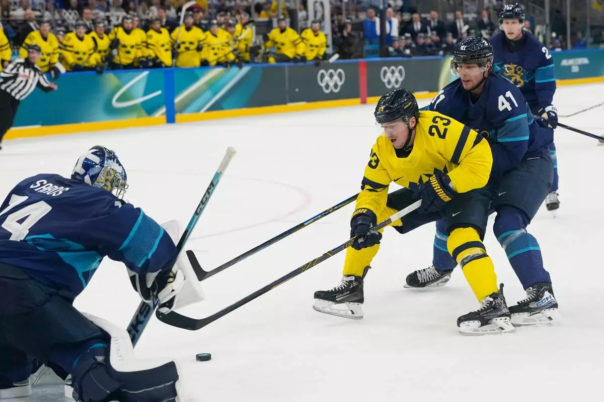 Finland's Miro Heiskanen, right, challenges Sweden's Lucas Raymond, center, as he tries to score past Finland's goalkeeper Juuse Saros during a preliminary round match of men's ice hockey between Finland and Sweden at the 2026 Winter Olympics, in Milan, Italy, Friday, Feb. 13, 2026. (AP Photo/Hassan Ammar)