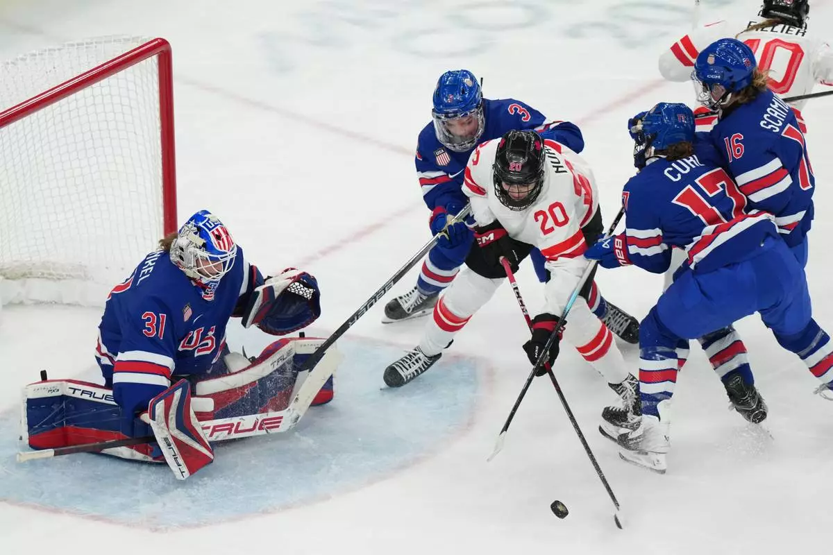 Canada's Sarah Nurse (20) is defended by United States' Cayla Barnes (3) and Britta Curl (17) as she tries to control the puck in front of goalkeeper Aerin Frankel (31) during the second period of the women's ice hockey gold medal game at the 2026 Winter Olympics, in Milan, Italy, Thursday, Feb. 19, 2026. (AP Photo/Carolyn Kaster)