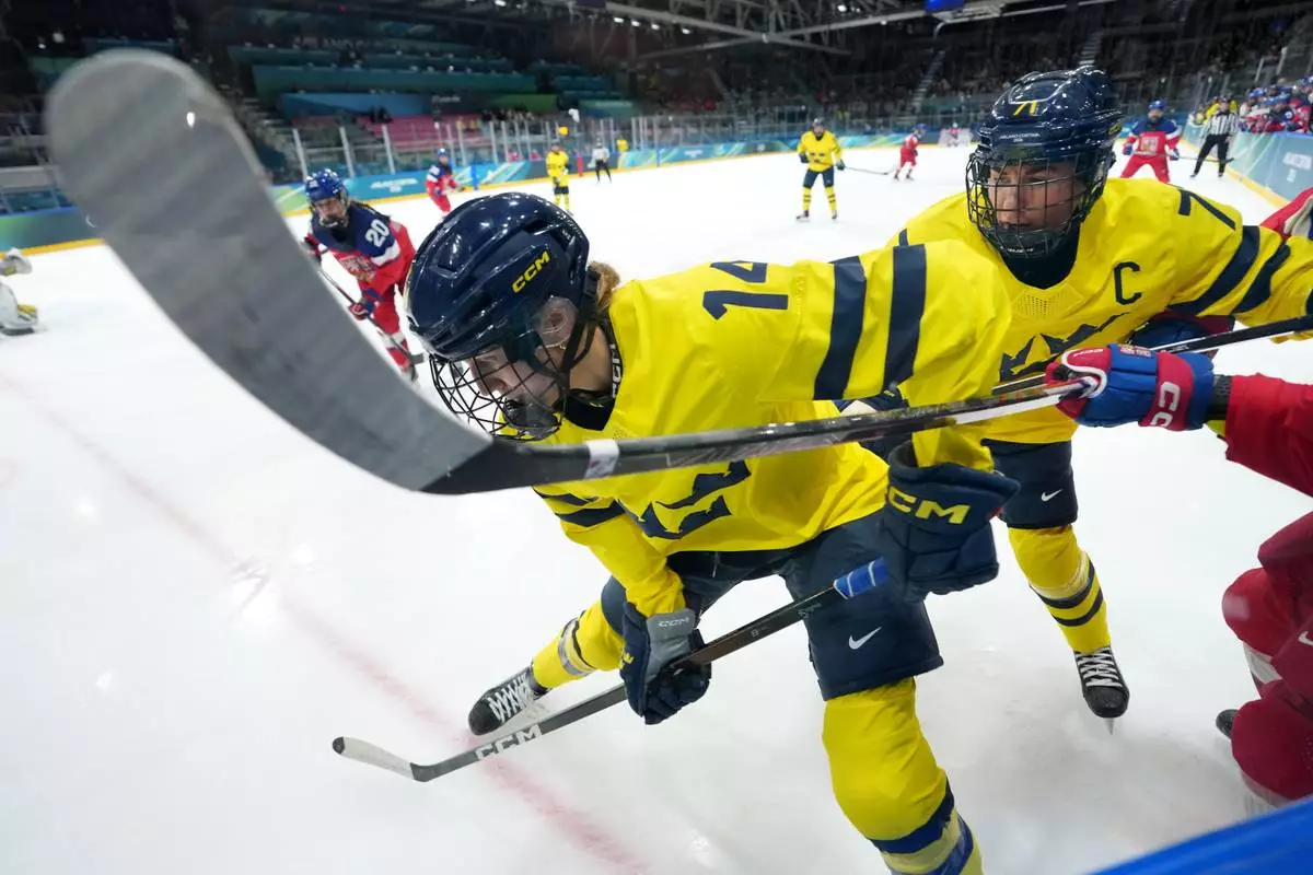 Sweden's Ida Karlsson (14) and Anna Kjellbin (71) try to clear the puck out of the corner during the second period of a women's ice hockey quarterfinal match between Sweden and Czechia at the 2026 Winter Olympics, in Milan, Italy, Friday, Feb. 13, 2026. (AP Photo/Carolyn Kaster)