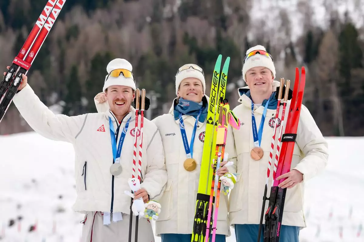 Gold medalist Johannes Hoesflot Klaebo, center, of Norway, poses flanked by silver medalist Ben Ogden, of the United States, left, and bronze medalist Oskar Opstad Vike, of Norway, on the podium of the cross-country skiing men's sprint classic at the 2026 Winter Olympics, in Tesero, Italy, Tuesday, Feb. 10, 2026. (AP Photo/Evgeniy Maloletka)