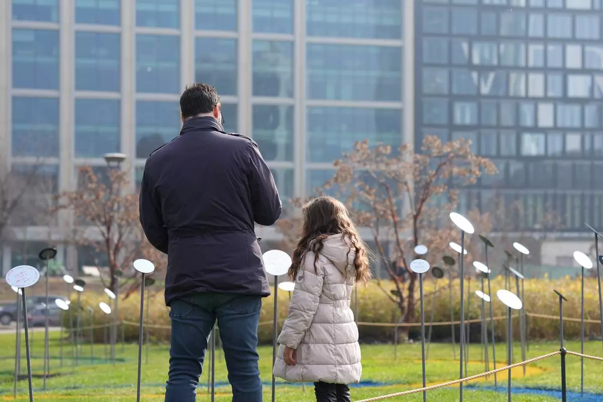 Anthony Cardamone walks with his daughter among mirrored flowers during “Together to Reflect,” an interactive community art project by BAM, the acronym for Biblioteca degli Alberi Milano, a public park in central Milan inviting the public to share thoughts on the values of sport, during the 2026 Winter Olympics, in Milan, Italy, Sunday, Feb. 8, 2026. (AP Photo/María Teresa Hernández)