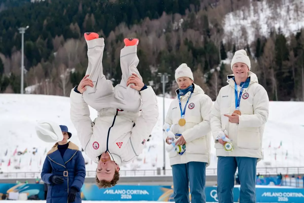 Silver medalist Ben Ogden, of the United States, does a back flip from the podium while gold medalist Johannes Hoesflot Klaebo, of Norway, and bronze medalist Oskar Opstad Vike, also of Norway, right, look on after the cross-country skiing men's sprint classic at the 2026 Winter Olympics, in Tesero, Italy, Tuesday, Feb. 10, 2026. (AP Photo/Evgeniy Maloletka)