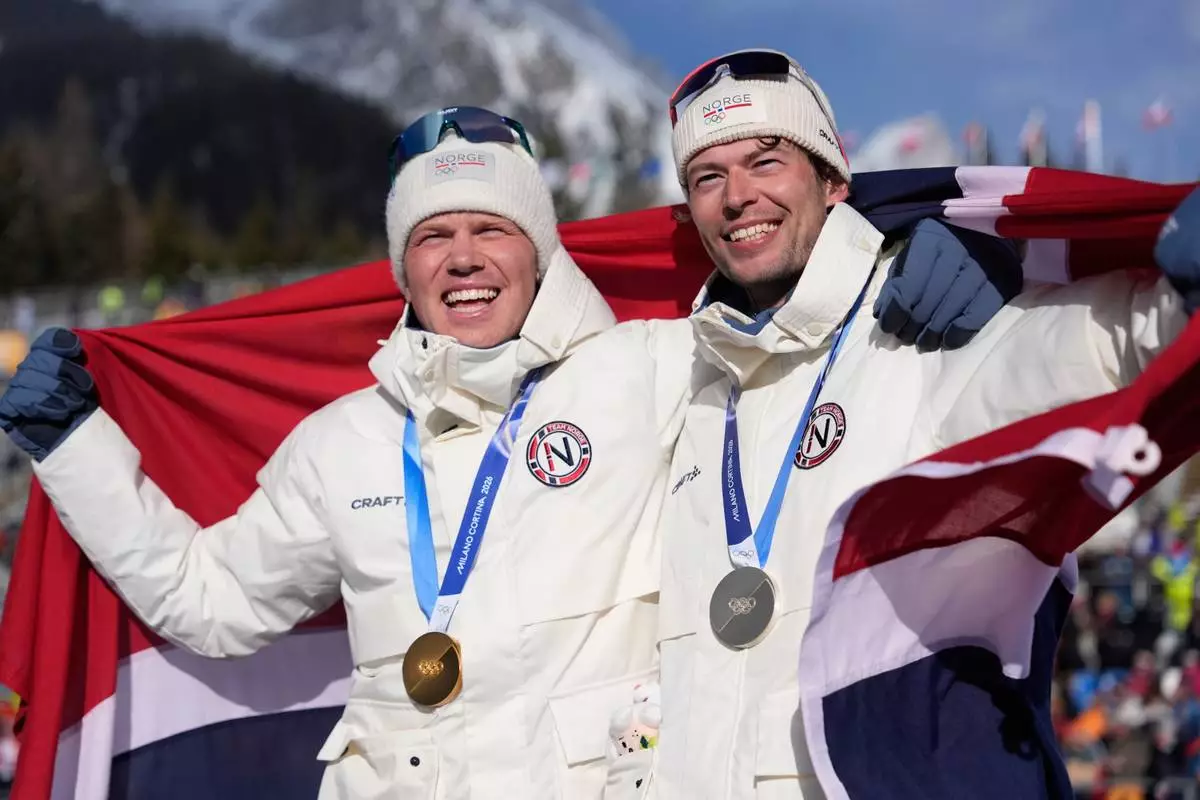 Gold medalist Johannes Dale-Skjevdal, of Norway, left, and silver medalist Sturla Holm Laegreid, of Norway, pose for photos after the men's 15-kilometer mass start biathlon race at the 2026 Winter Olympics in Anterselva, Italy, Friday, Feb. 20, 2026. (AP Photo/Mosa'ab Elshamy)