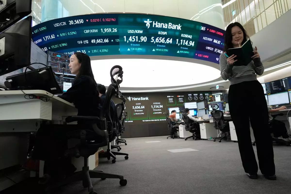 Currency traders work near a screen showing the Korea Composite Stock Price Index (KOSPI), top center, and the foreign exchange rate between U.S. dollar and South Korean won, top center left, at the foreign exchange dealing room of the Hana Bank headquarters in Seoul, South Korea, Thursday, Feb. 19, 2026. (AP Photo/Ahn Young-joon)