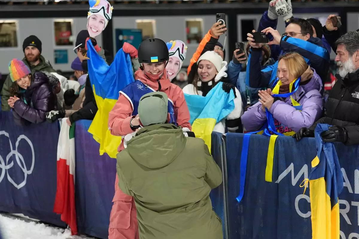 Ukraine's Kateryna Kotsar gets a proposal from Bogdan Fashtryga, front, as she competes in the women's freestyle skiing big air qualifications at the 2026 Winter Olympics, in Livigno, Italy, Saturday, Feb. 14, 2026. (AP Photo/Abbie Parr)