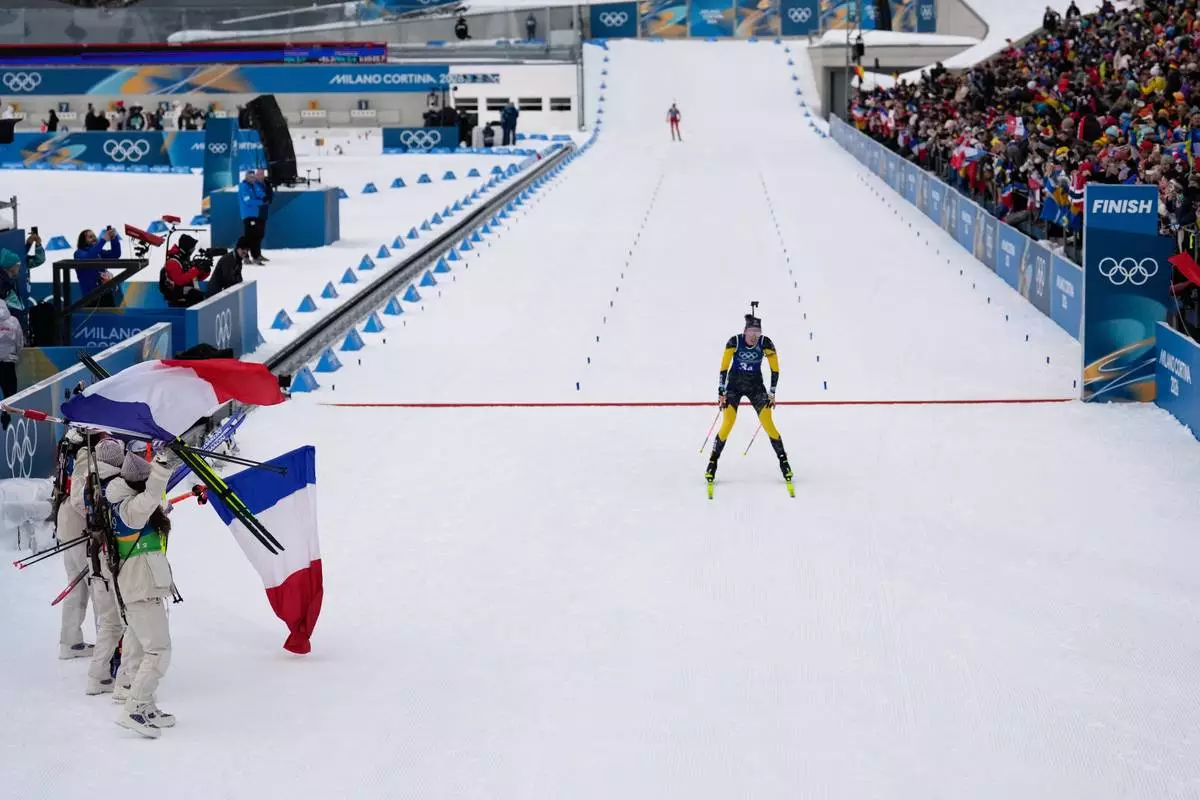 Members of Team France wave their country's flag as Hanna Oeberg, of Sweden, crosses the finish line for silver in the women's 4x6-kilometer relay biathlon race at the 2026 Winter Olympics in Anterselva, Italy, Wednesday, Feb. 18, 2026. (AP Photo/Mosa'ab Elshamy)