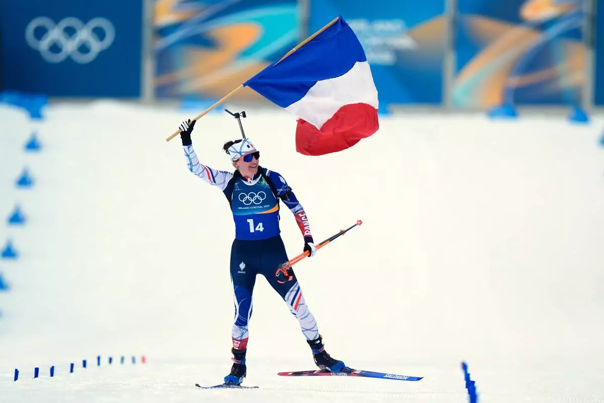 Julia Simon, of France, skis to the finish line with her country's flag for gold in the women's 4x6-kilometer relay biathlon race at the 2026 Winter Olympics in Anterselva, Italy, Wednesday, Feb. 18, 2026. (AP Photo/Andrew Medichini)