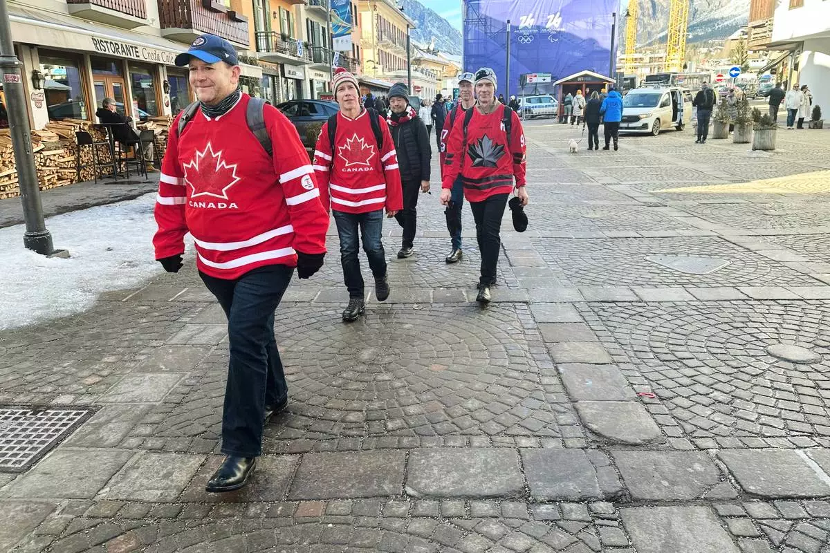 Dan Wilton, of Vancouver, Canada, left walks with his friends without jackets as temperatures rise in the host city, during the 2026 Winter Olympics in Cortina d'Ampezzo, Italy, Sunday, Feb. 8, 2026. (AP Photo/ Jennifer McDermott)