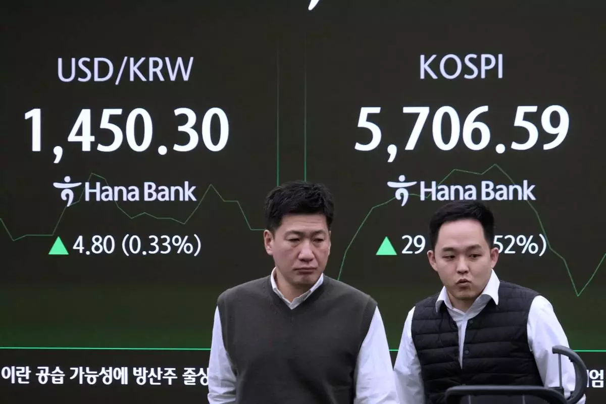Currency traders pass by a screen showing the Korea Composite Stock Price Index (KOSPI), right, and the foreign exchange rate between U.S. dollar and South Korean won at the foreign exchange dealing room of the Hana Bank headquarters in Seoul, South Korea, Friday, Feb. 20, 2026. (AP Photo/Ahn Young-joon)