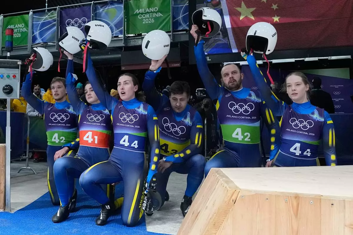 Ukraine's Yulianna Tunytska, Olena Stetskiv, Oleksandra Mokh, Nazarii Kachmar, Ihor Hoi and Andriy Mandziy kneel down during the luge relay competition at the 2026 Winter Olympics, in Cortina d'Ampezzo, Italy, Thursday, Feb. 12, 2026. (AP Photo/Alessandra Tarantino)
