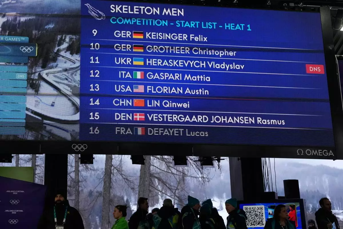 A scoreboard, that indicates that Ukrainian skeleton athlete Vladyslav Heraskevych did not start, is seen at the 2026 Winter Olympics, in Cortina d'Ampezzo, Italy, Thursday, Feb. 12, 2026. (AP Photo/Alessandra Tarantino)