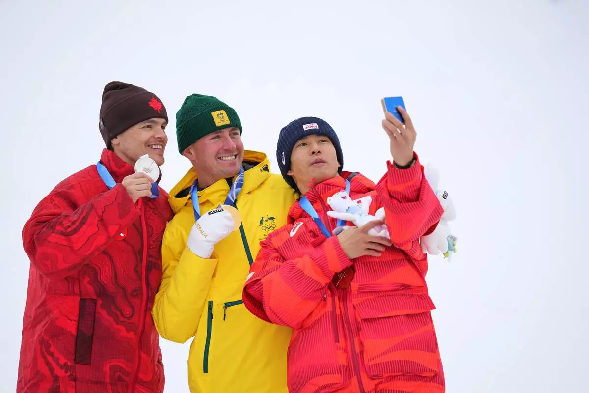 From left, silver medalist Canada's Mikael Kingsbury, gold medalist Australia's Cooper Woods and bronze medalist Japan's Ikuma Horishima take a selfie after the men's freestyle skiing moguls finals at the 2026 Winter Olympics, in Livigno, Italy, Thursday, Feb. 12, 2026. (AP Photo/Abbie Parr)