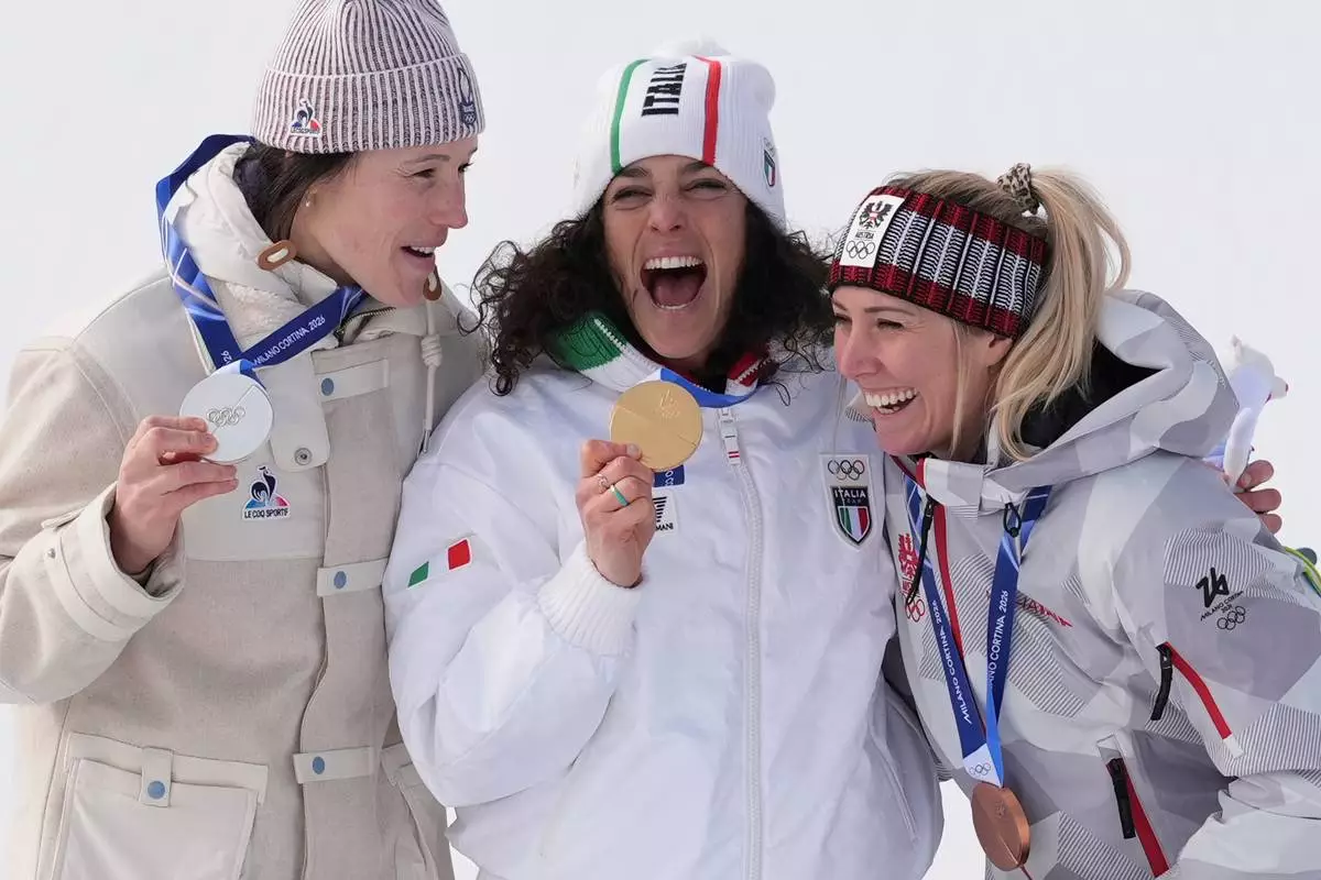 Italy's Federica Brignone, center, gold medalist in an alpine ski, women's super-G race, celebrates with silver medalist France's Romane Miradoli, left, and bronze medalist Austria's Cornelia Huetter, at the 2026 Winter Olympics, in Cortina d'Ampezzo, Italy, Thursday, Feb. 12, 2026. (AP Photo/Jacquelyn Martin)