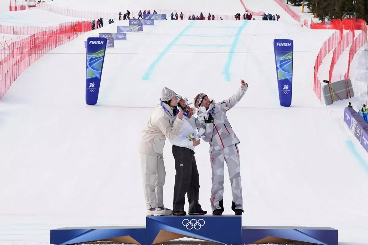 Italy's Federica Brignone, center, gold medalist in an alpine ski, women's super-G race, silver medalist France's Romane Miradoli, left, and bronze medalist Austria's Cornelia Huetter, take a selfie at the 2026 Winter Olympics, in Cortina d'Ampezzo, Italy, Thursday, Feb. 12, 2026. (AP Photo/Jacquelyn Martin)