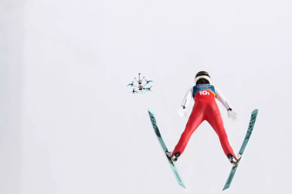 A drone follows Lisa Eder, of Austria, soaring through the air during the ski jumping mixed team competition at the 2026 Winter Olympics, in Predazzo, Italy, Tuesday, Feb. 10, 2026. (AP Photo/Evgeniy Maloletka)
