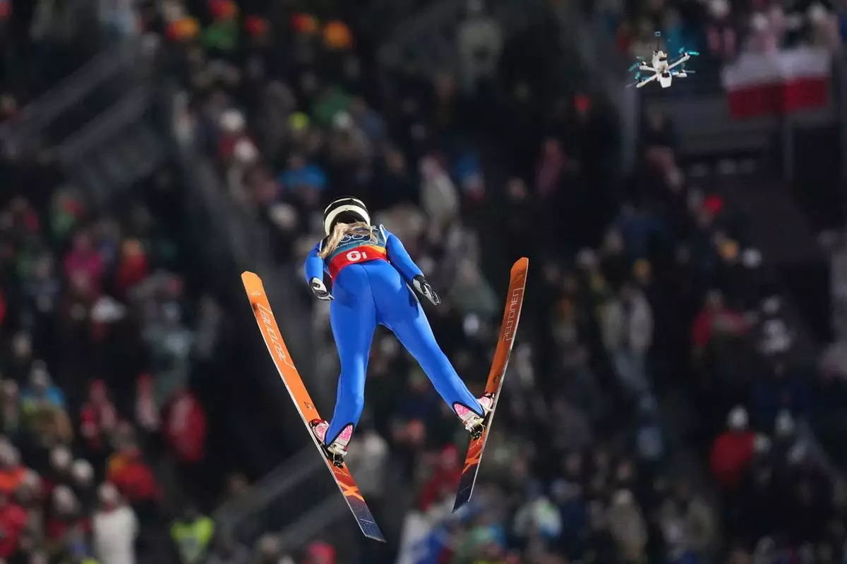 A drone follows Heta Hirvonen, of Finland, soaring through the air during the ski jumping mixed team competition at the 2026 Winter Olympics, in Predazzo, Italy, Tuesday, Feb. 10, 2026. (AP Photo/Evgeniy Maloletka)