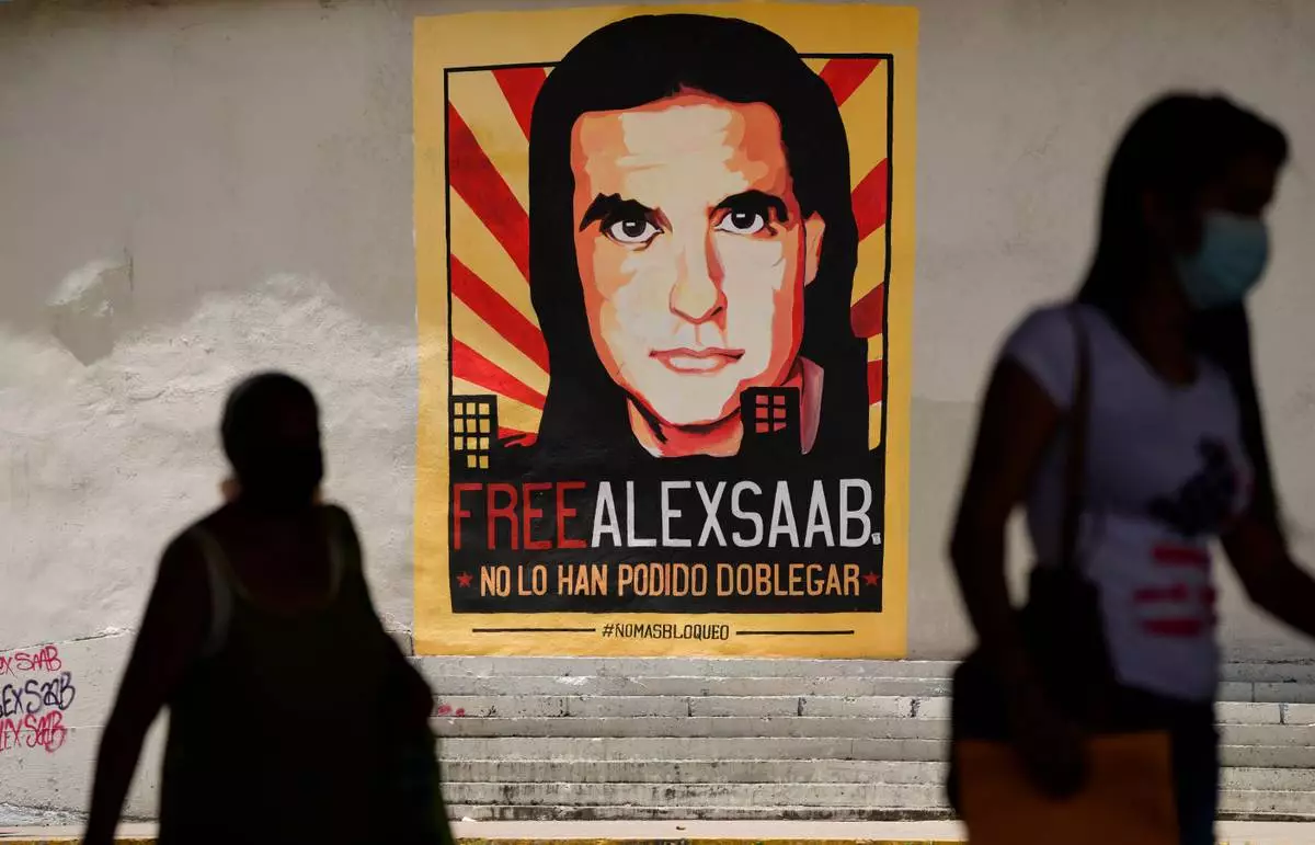 FILE - Pedestrians walk near a poster asking for the freedom of Colombian businessman and Venezuelan special envoy Alex Saab, in Caracas, Venezuela, Sept. 9, 2021. (AP Photo/Ariana Cubillos, File)