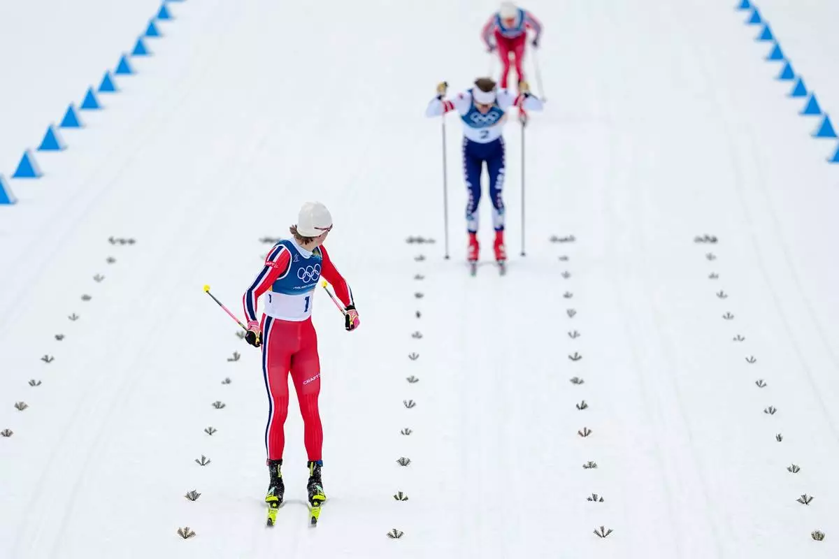 Gold medalist Johannes Hoesflot Klaebo, left, of Norway, looks back at silver medalist Ben Ogden, of the United States, and bronze medalist Oskar Opstad Vike, also of Norway, when approaching the finish line in the cross-country skiing men's sprint classic at the 2026 Winter Olympics, in Tesero, Italy, Tuesday, Feb. 10, 2026. (AP Photo/Matthias Schrader)