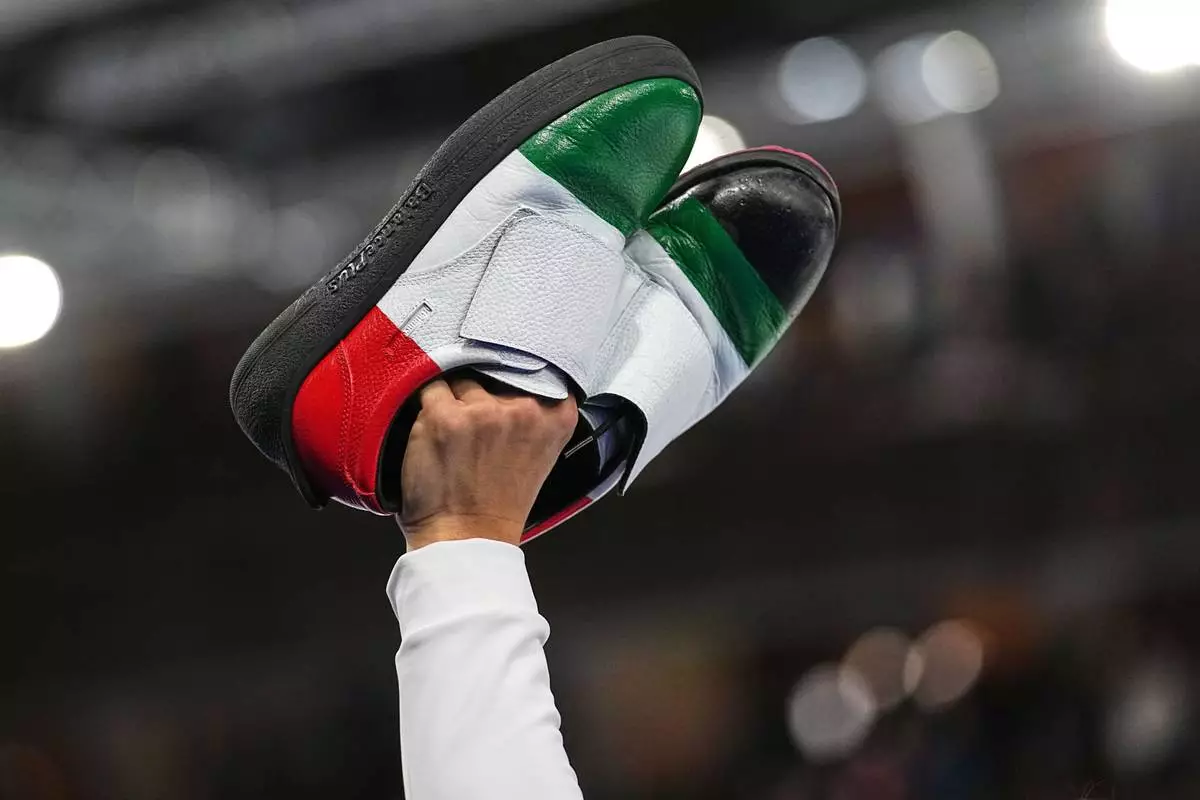 Italy's Mattia Giovanella gestures holding his shoes, after the men's curling round robin session against Britain, at the 2026 Winter Olympics, in Cortina d'Ampezzo, Italy, Friday, Feb. 13, 2026. (AP Photo/Fatima Shbair)