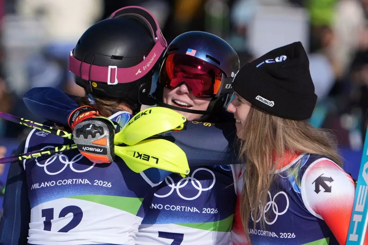 United States' Mikaela Shiffrin, center, winner of an alpine ski, women's slalom race, is congratulated by second-placed Switzerland's Camille Rast, right, and third-placed Sweden's Anna Swenn Larsson, at the 2026 Winter Olympics, in Cortina d'Ampezzo, Italy, Wednesday, Feb. 18, 2026. (AP Photo/Jacquelyn Martin)