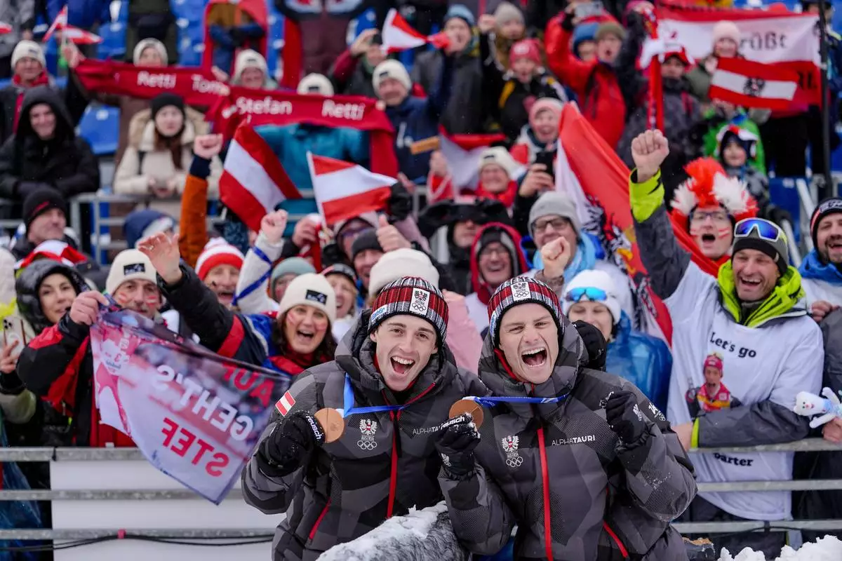 Stefan Rettenegger, left, and Johannes Lamparter, of Austria, pose with supporters after winning the bronze medal in the nordic combined team sprint at the 2026 Winter Olympics, in Tesero, Italy, Thursday, Feb. 19, 2026. (AP Photo/Matthias Schrader)