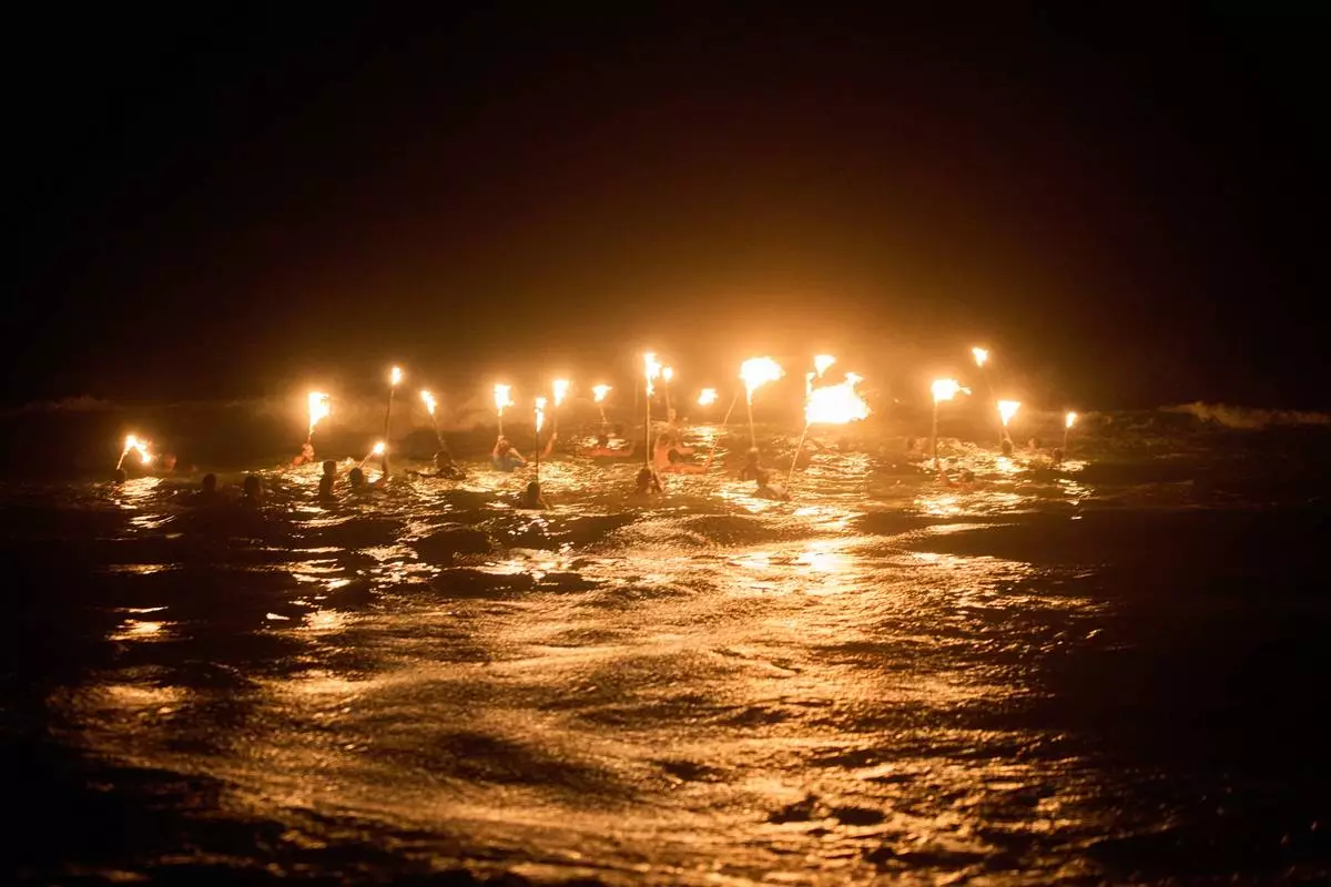 Lifeguards holding torches, wade into the Atlantic ocean in a ceremony to commemorate Lifeguard Day, to honor their commitment to safety and aquatic rescue, in Mar Azul, Argentina, Saturday, Feb. 14, 2026. (AP Photo/Rodrigo Abd)