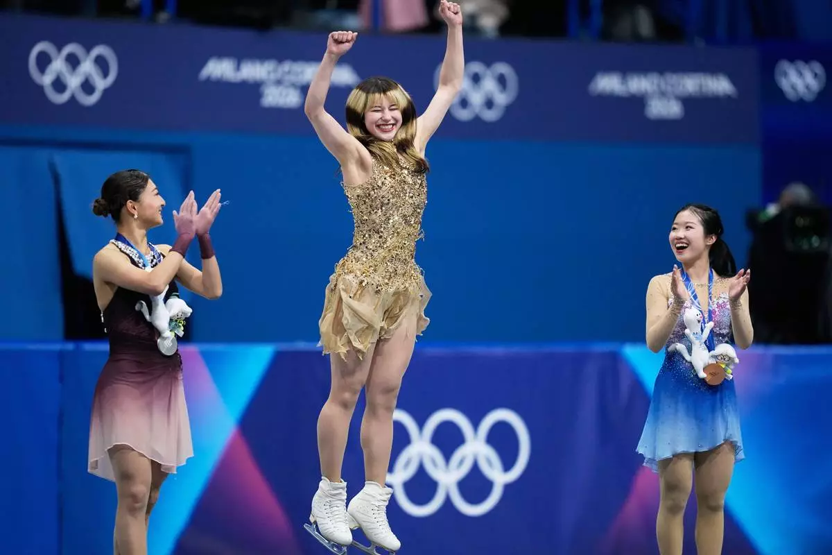 From left to right, silver medalist Kaori Sakamoto of Japan, gold medalist Alysa Liu of the United States, and bronze medalist Ami Nakai of Japan, jump on the podium to receive their medals after competing in the women's free skate program in figure skating at the 2026 Winter Olympics, in Milan, Italy, Thursday, Feb. 19, 2026. (AP Photo/Natacha Pisarenko)