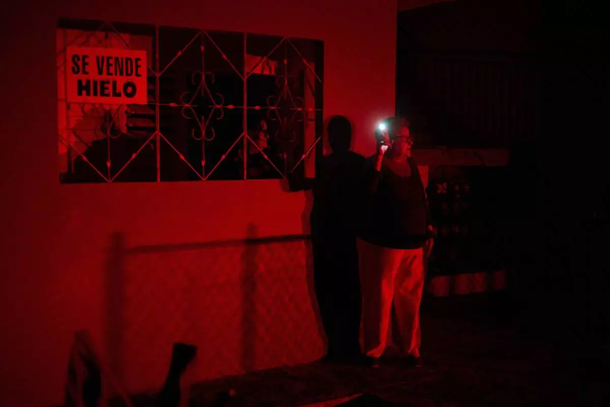 FILE - A woman holds up a cell phone flashlight as she chats with a friend during a scheduled power outage as part of energy rationing in Santa Cruz del Norte, home to one of Cuba's largest thermoelectric plants, Feb. 3, 2026. (AP Photo/Ramon Espinosa, File)