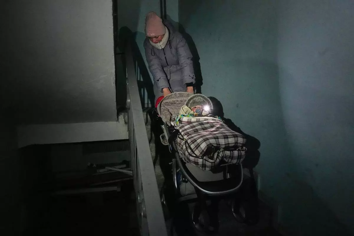 FILE - Yuliia Dolotova pulls her son in a stroller up apartment stairs during a power outage caused by Russia's repeated air strikes on the country's power grid, in Kyiv, Ukraine, Feb. 2, 2026. (AP Photo/Sergey Grits, File)