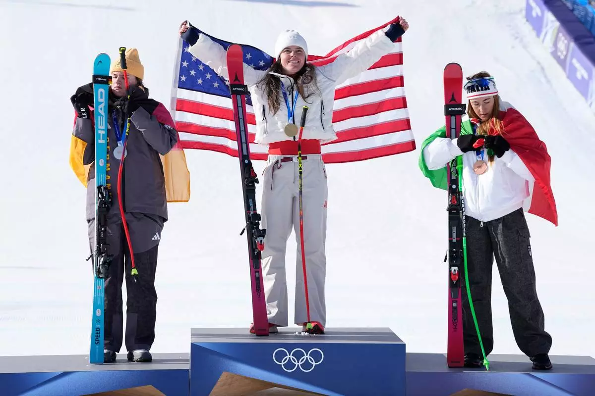 United States' Breezy Johnson, center, gold medal in an alpine ski women's downhill race, celebrates on the podium with silver medalist Germany's Emma Aicher, left, and bronze medalist Italy's Sofia Goggia, at the 2026 Winter Olympics, in Cortina d'Ampezzo, Italy, Sunday, Feb. 8, 2026. (AP Photo/Andy Wong)